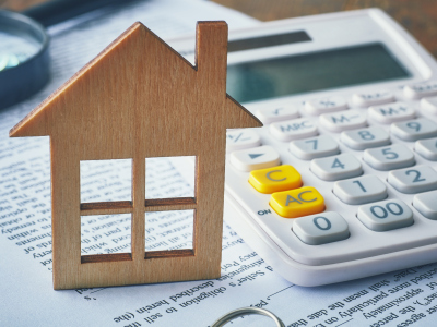 En kalkulator og en liten trefigur av et hus er plassert oppå papirer på et bord. Foto