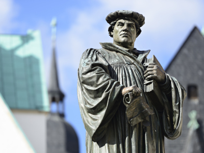 Martin Luther i hans fødeby, Eisleben i Tyskland. Han har på seg en kappe og holder en bok. Han ser bestemt ut i lufta. Foto