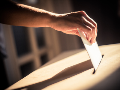 En hånd legger en stemmeseddel inn i en stemmeurne. Foto