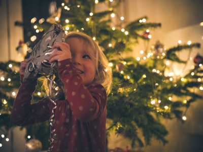Jente holder en julegave. Juletre med lys i bakgrunnen. Foto.