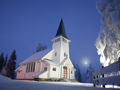 En hvit kirke i snøen. Det er mørkt utenfor. Foto
