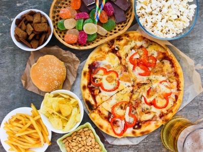 Pizza, pommes fritt, godteri, popcorn, hamburger og øl på et bord. Bildet viser usunn mat. Foto