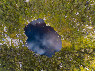 En liten innsjø inne i en skog. Bildet er tatt ovenifra. Foto