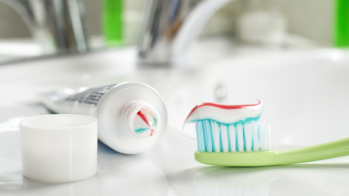 En tannbørste ligger ved en vask. Det er tannkrem på tannbørsten, og den er klar til bruk. Foto