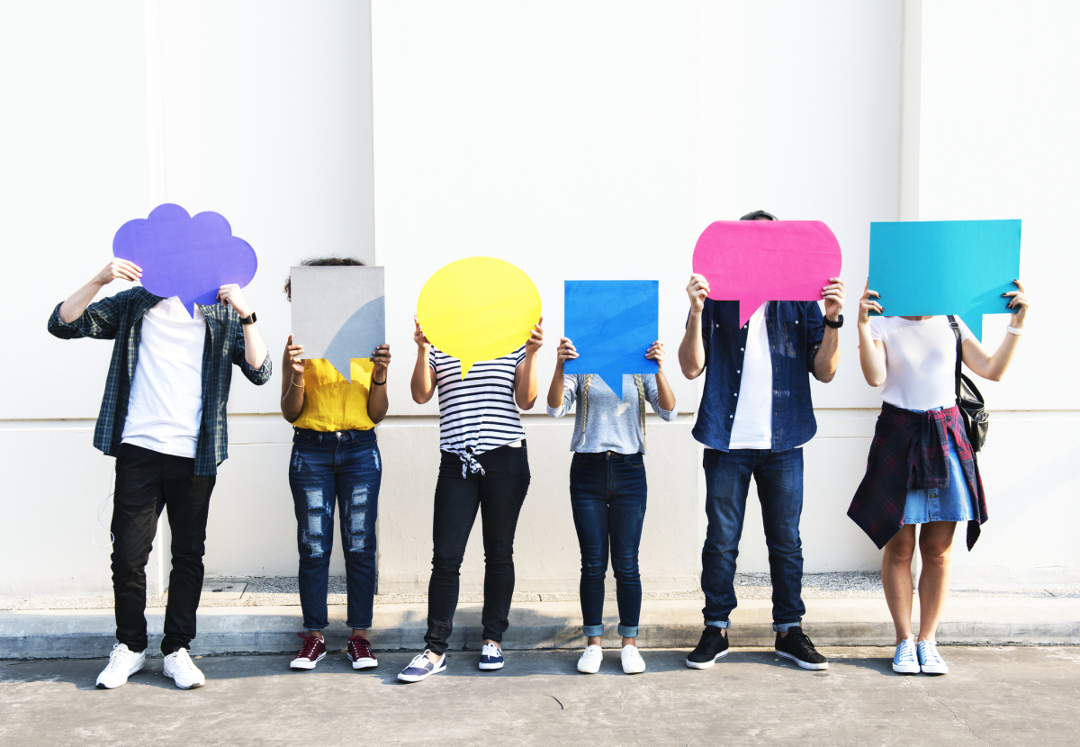 Seks personer står ved siden av hverandre. De holder opp tankebobler og snakkebobler laget med papir i forskjellige farger. Bildet illustrerer at de har forskjellige meninger. Foto