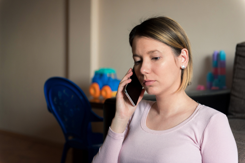 En bekymret og alvorspreget kvinne holder telefonen til øret. Bildet illustrerer en kvinne som oppsøker hjelp etter å ha blitt utsatt for vold i hjemmet. Foto